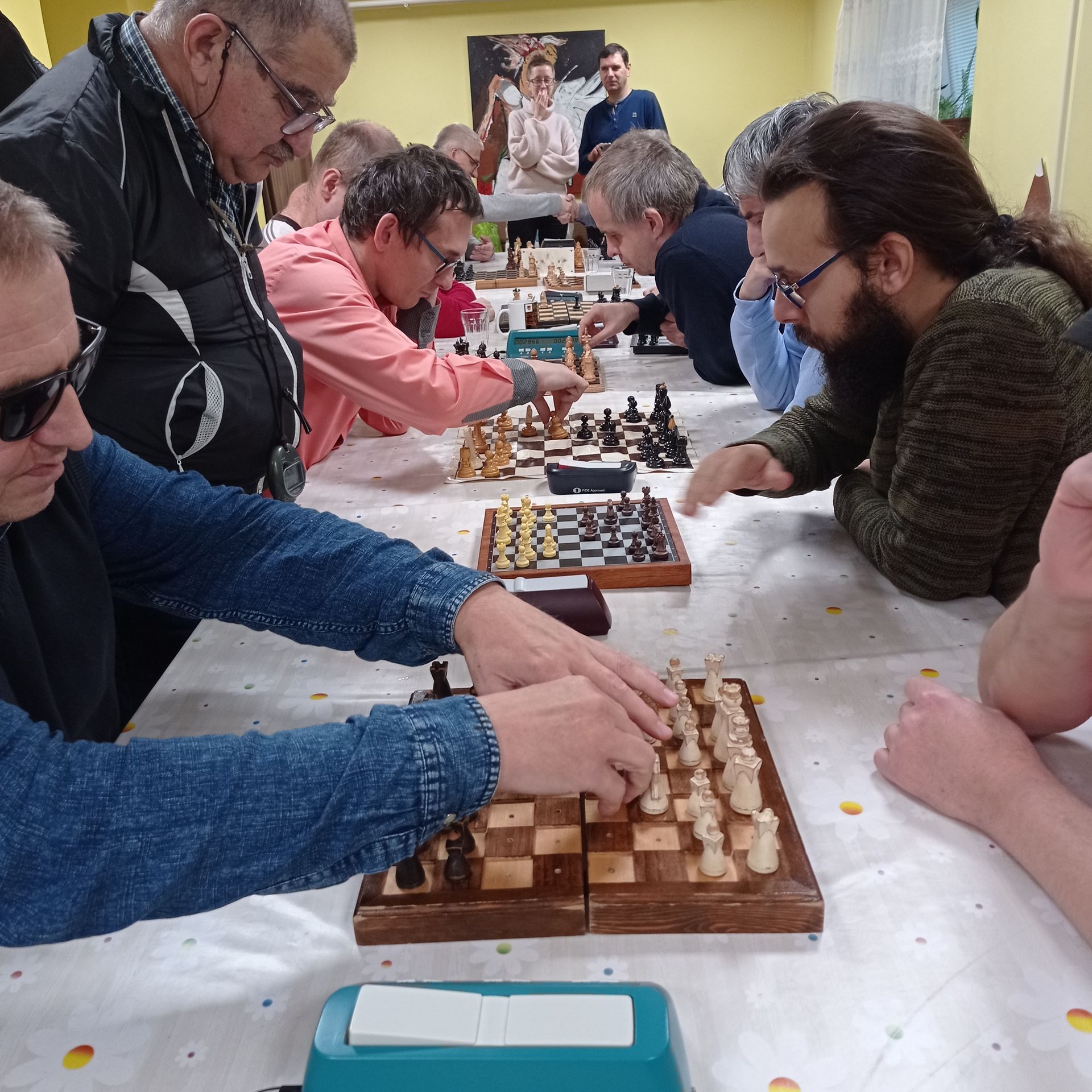 Bližší záber na hráčov, šachovnice a rozohrané partie medzi nimi. Na fotografii je niekoľko hráčov šachu a záber na šachovnice s figúrkami.