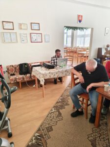 Skupina ľudí, ktorá sedí v miesnosti a počúva prednášajúcu osobu.