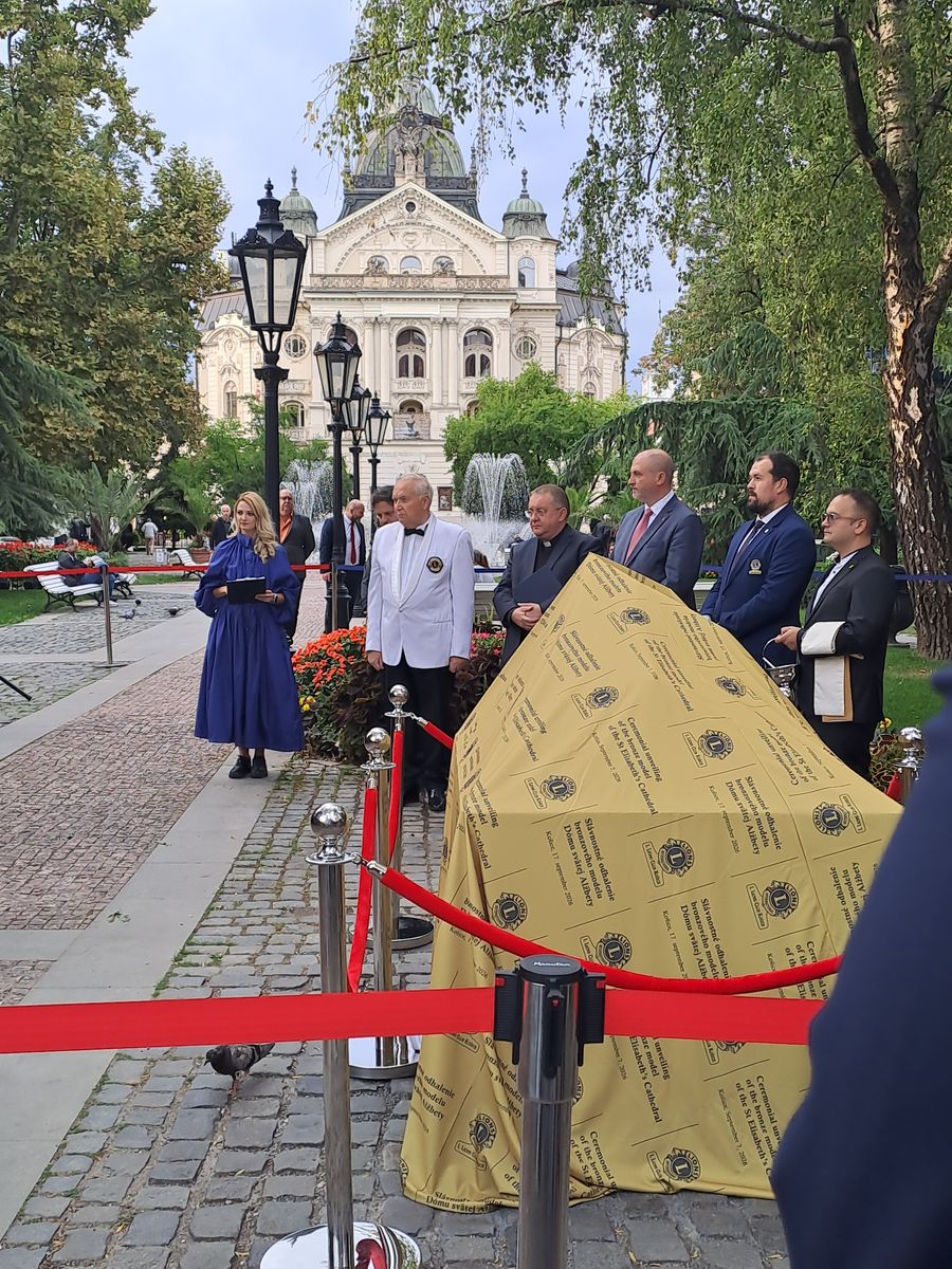 Záber na zahalenú maketu a účastníkov.